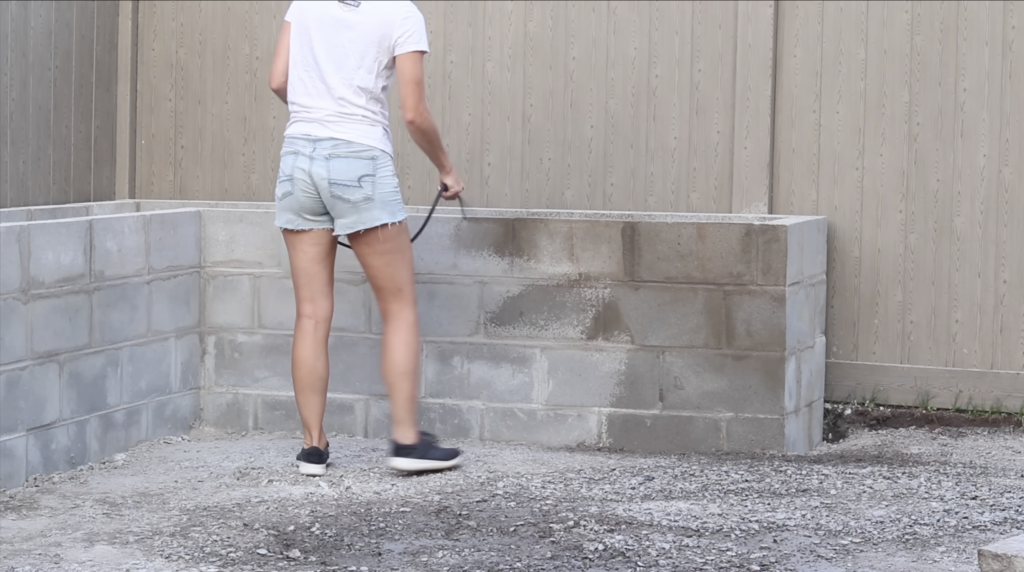 spraying down the cinder blocks on the DIY Raised Concrete Garden Bed